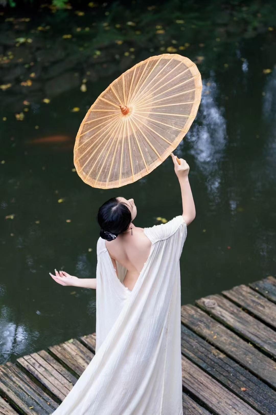 露背白裙女性于水边木栈道高举油纸伞